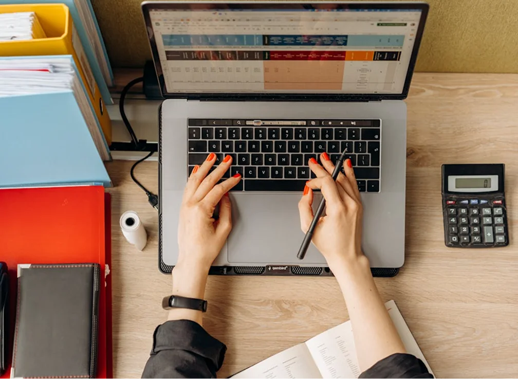 A person with red nails typing on a laptop while holding a pen
